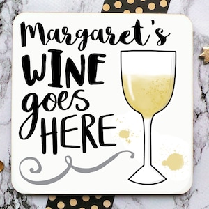 Puede incluir: Posavasos blanco con texto negro que dice "Margaret's Wine goes HERE" y un contorno negro de una copa de vino blanco. La copa est&aacute; llena de un l&iacute;quido amarillo claro.