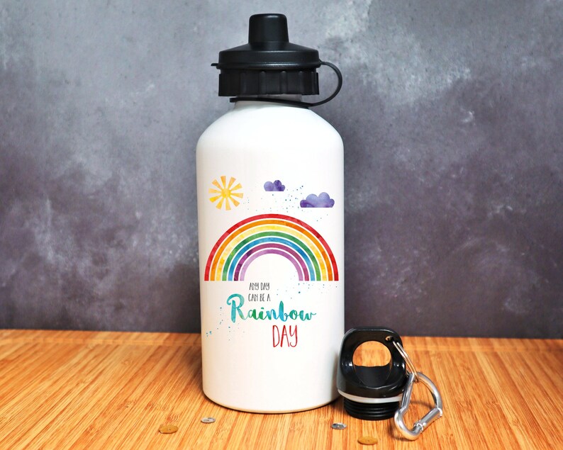 Puede incluir: Botella de agua de aluminio blanca con un arco&iacute;ris, nubes y un sol. El texto "Any day can be a Rainbow Day" est&aacute; impreso en la botella.