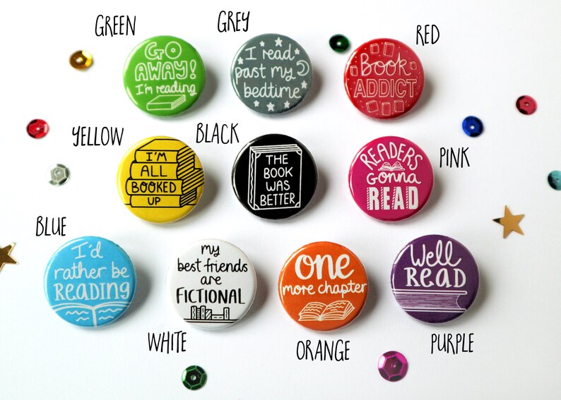 May include: Ten round button pins with various book-themed sayings. The buttons are in different colors, including green, grey, black, red, pink, blue, white, orange, and purple.