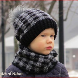 May include: A child wearing a black and grey checkered knit hat with a faux fur pom pom and a matching scarf. The hat and scarf are crocheted.