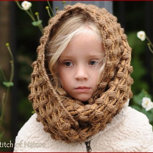May include: A young girl wearing a brown and tan crocheted infinity scarf with a textured pattern. The scarf is worn as a cowl and covers the girl's neck and head.