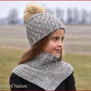 Pode incluir: Um chapéu de crochê cinza e branco com um pompom felpudo e um cachecol de crochê cinza e branco combinando.