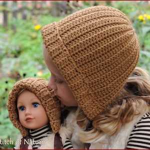 May include: Two children wearing brown crocheted hats with hoods. The child on the left is a doll with blue eyes. The child on the right is a young girl with long blonde hair.