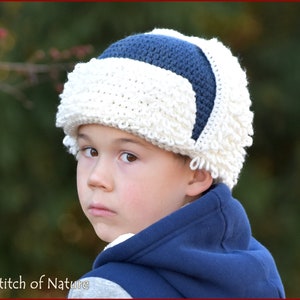 May include: A young child wearing a white and blue crocheted hat with a fluffy brim. The hat has a blue stripe across the top.