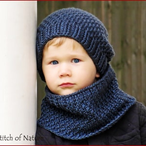 May include: A young child wearing a blue knitted hat and matching scarf. The hat has a slouchy fit and the scarf is a cowl style.