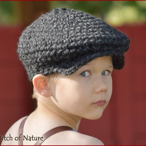 Puede incluir: Una persona joven con una gorra de newsboy de punto gris. La gorra tiene una parte superior plana y un ala que se curva hacia abajo alrededor de las orejas.