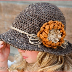 May include: A brown crocheted hat with a large brown and orange crocheted flower on the side. The hat has a wide brim and is tied with a brown twine.