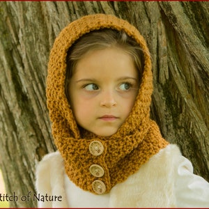 May include: A young girl wearing a brown crocheted hooded cowl with wooden buttons. The cowl is worn over a white vest. The girl is standing next to a tree trunk.
