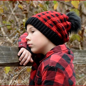 May include: A red and black crocheted beanie with a black faux fur pom pom. The beanie is worn by a person wearing a red and black plaid shirt.