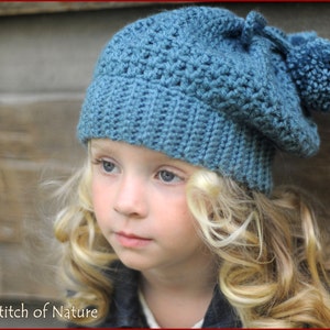 May include: A young person wearing a blue crocheted beanie with a pom-pom on top. The beanie has a textured stitch pattern.