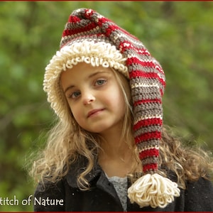 May include: A young girl wearing a red, white and brown striped crocheted hat with a long, pointed tip and a white pom-pom. The hat has a white crocheted trim around the brim.