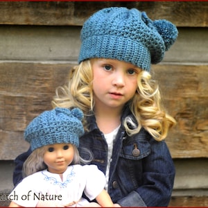 May include: A young girl wearing a blue crocheted beanie with a pom-pom on top, holding a doll wearing a matching blue crocheted beanie. The girl is wearing a denim jacket and the doll is wearing a white dress with embroidery. The background is a wooden wall.