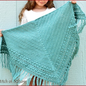 May include: A teal crochet shawl with fringe. The shawl is made with a textured stitch and has a delicate pattern. Stitch of Nature is written on the bottom left corner of the image.