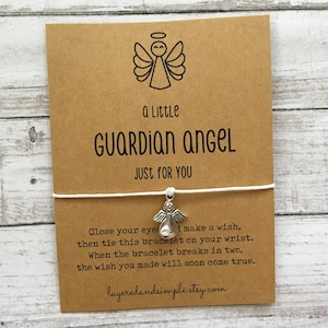Puede incluir: Una tarjeta marr&oacute;n con el texto "a Little GUARDIAN ANGEL JUST FOR YOU" y una ilustraci&oacute;n de un &aacute;ngel. Una cuerda blanca con un dije de &aacute;ngel plateado est&aacute; adjunta. La tarjeta incluye instrucciones.