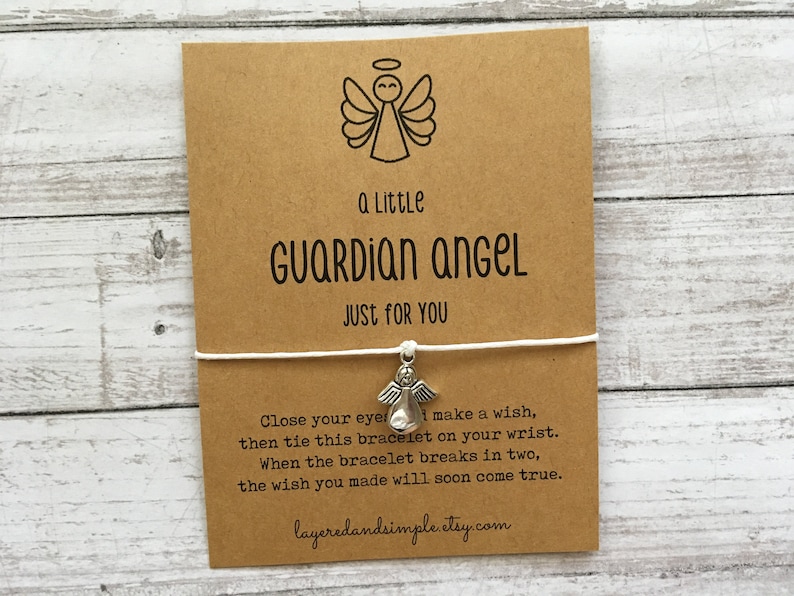 Puede incluir: Una tarjeta marr&oacute;n con el texto "a Little GUARDIAN ANGEL JUST FOR YOU" y una ilustraci&oacute;n de un &aacute;ngel. Una cuerda blanca con un dije de &aacute;ngel plateado est&aacute; adjunta. La tarjeta incluye instrucciones.