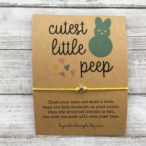 May include: A yellow friendship bracelet with a silver star charm and a card that reads "cutest little peep" with a green peep illustration. The card also includes instructions for making a wish and tying the bracelet.