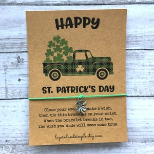 May include: A green and black truck with a bed full of shamrocks. The truck is on a brown card with the text "HAPPY" and "ST. PATRICK'S DAY". The card also includes instructions for a wish bracelet: "Close your eyes make a wish, then tie this bracelet on your wrist. When the bracelet breaks in two, the wish you made will soon come true." The card also includes the website layeredandsimple.etsy.com.