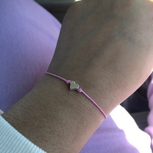 May include: A pink string bracelet with a silver heart charm.