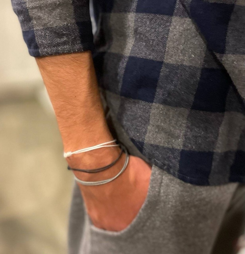 May include: A person wearing a blue and gray plaid shirt with three bracelets on their wrist. The bracelets are white, black, and gray.