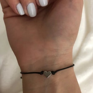 May include: A simple black string bracelet with a small silver heart charm.