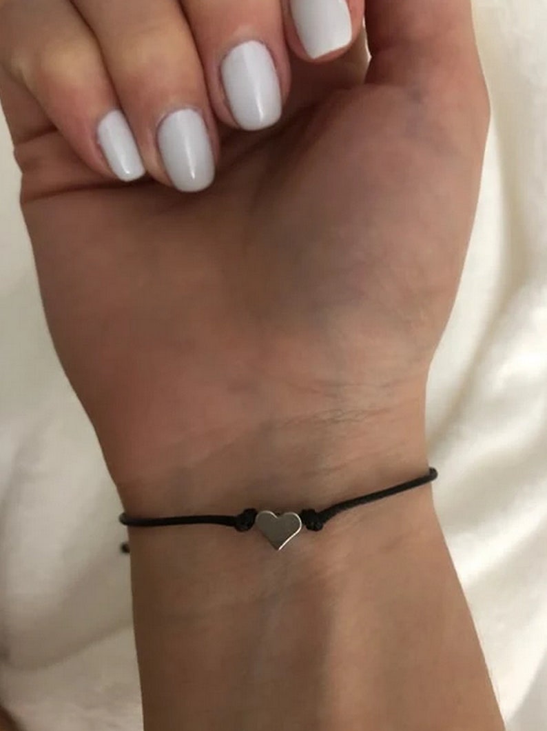 May include: A simple black string bracelet with a small silver heart charm.