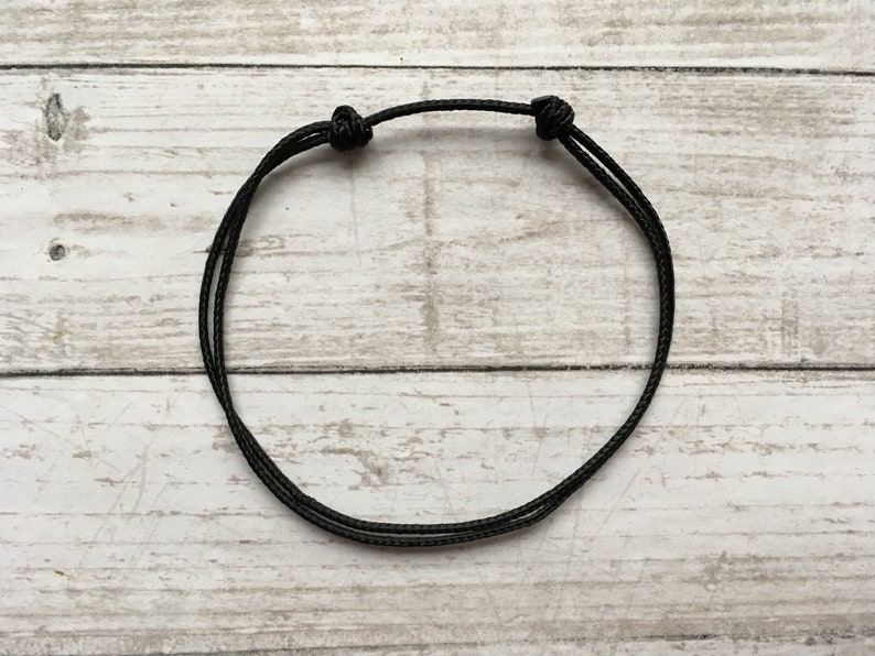 May include: A simple black cord bracelet with two knots on either side.