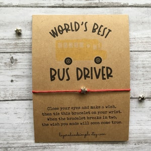 May include: A brown card with the text "WORLD'S BEST BUS DRIVER" and a yellow school bus illustration. A red string bracelet with a silver star charm is attached to the card. The card also includes the text "Close your eyes and make a wish, then tie this bracelet on your wrist. When the bracelet breaks in two, the wish you made will soon come true." and the website "layeredandsimple.etsy.com".