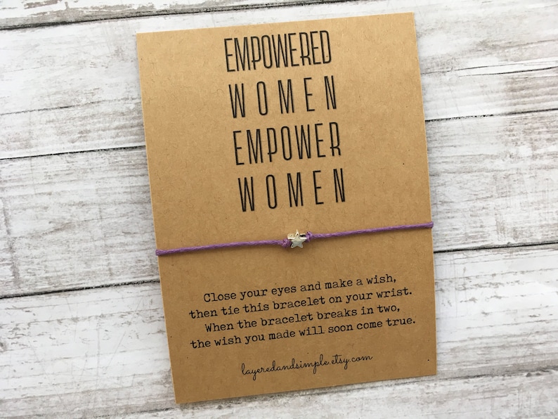 May include: A brown card with the text "EMPOWERED WOMEN EMPOWER WOMEN" and a purple string bracelet with a silver star charm. The card also includes instructions for making a wish with the bracelet.