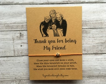 May include: A brown card with a black and white image of four women. The card says "Thank you for being My Friend". Below the card is a string bracelet with a silver star charm. The bracelet has the following text: "Close your eyes and make a wish, then tie this bracelet on your wrist. When the bracelet breaks in two, the wish you made will soon come true."