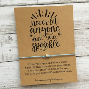 May include: A brown card with the text "never let anyone *dull your* sparkle" and a blue string bracelet with silver star charms. The card also includes instructions for making a wish with the bracelet.
