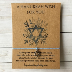 May include: A Hanukkah wish card with a Star of David design and the text "A Hanukkah Wish For You." The card includes a light blue bracelet with a Star of David charm. The card also has text that reads "Close your eye..." and the Etsy shop name.