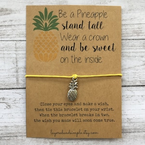 May include: A kraft paper card with a yellow string bracelet and a silver pineapple charm. The card features a pineapple graphic and the text "Be a Pineapple, stand tall, Wear a crown and be sweet on the inside."