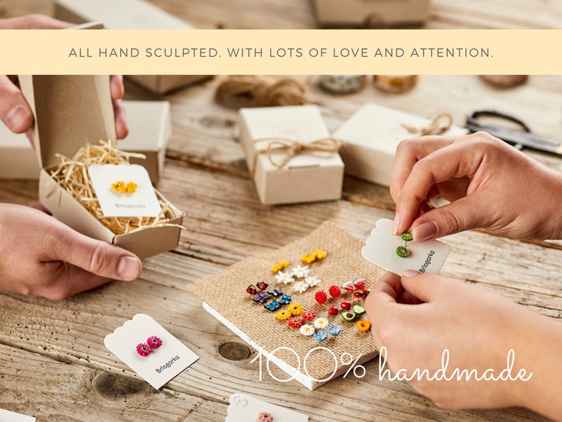 May include: A collection of colorful, handmade earrings displayed on a wooden surface. The image shows various floral and fruit designs, with some earrings packaged in small boxes. Text on the image reads "ALL HAND SCULPTED. WITH LOTS OF LOVE AND ATTENTION." and "100% handmade."