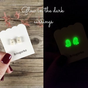Può includere: Un paio di orecchini bianchi a forma di fantasma su una carta bianca, con il testo "Glow in the dark earrings". Gli orecchini si illuminano di verde al buio. La carta ha il nome del marchio "Brlogarka" stampato.