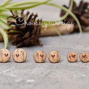 May include: Wooden stud earrings with a heart design in three sizes: 12mm, 10mm, and 8mm. The earrings are made of light brown cork material with a dark brown heart. The text "Choose your size" is in the background.