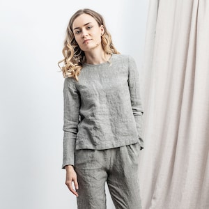 May include: A light gray linen outfit, consisting of a long-sleeved top and matching pants. The top has a textured pattern, and the pants have a relaxed fit. The outfit is worn with neutral-colored shoes.