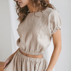 May include: A beige linen top and skirt set. The top has a round neckline and short sleeves. The skirt has an elastic waistband and a relaxed fit.