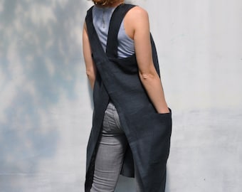 May include: A dark blue linen apron with a criss-cross back strap and two pockets. The apron is worn over a light blue tank top and gray jeans.