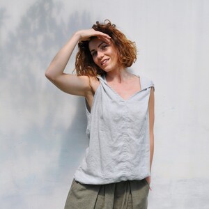 May include: A woman wearing a light gray sleeveless top with a v-neck and a pair of olive green linen pants.