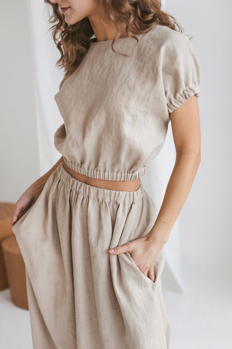 May include: A beige linen top and skirt set. The top has a round neckline and short sleeves. The skirt has an elastic waistband and a relaxed fit.