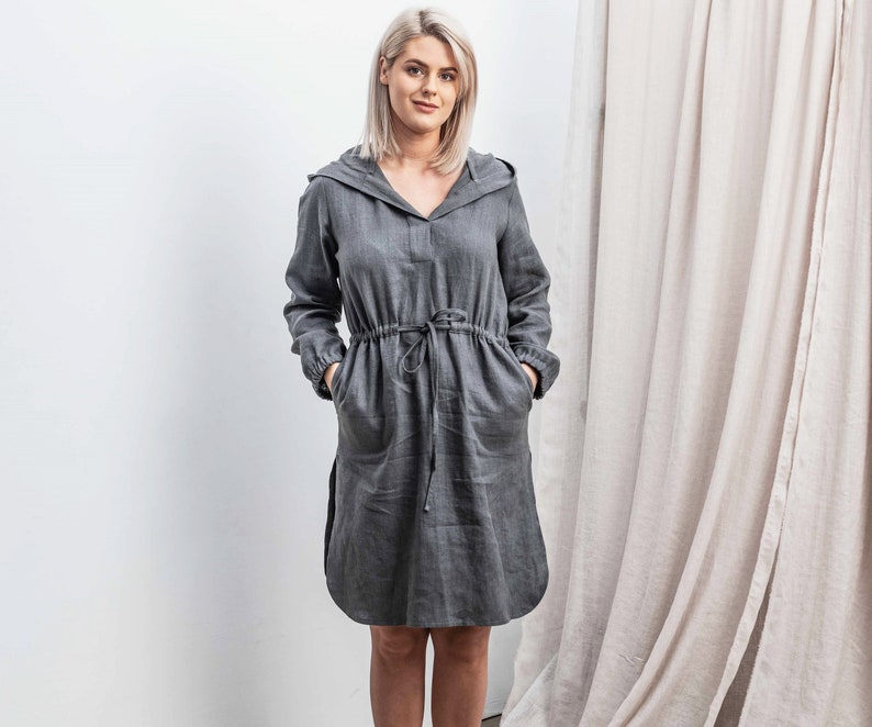 K&ouml;nnte beinhalten: Ein graues, kapuzenf&ouml;rmiges Leinenkleid mit einem Kordelzug in der Taille. Das Kleid hat eine lockere Passform und ist perfekt f&uuml;r Freizeitkleidung.