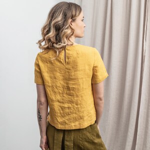 May include: A yellow linen top with short sleeves and a keyhole back detail. The top is made of a lightweight, breathable fabric and is perfect for warm weather.