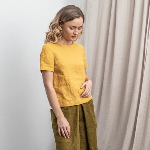 May include: A woman wearing a yellow linen top with short sleeves and a green linen skirt.