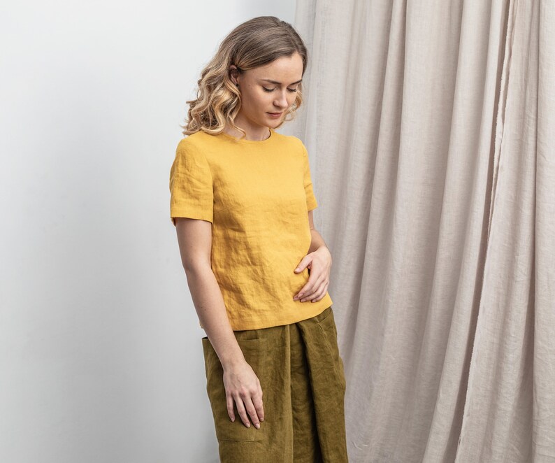 May include: A woman wearing a yellow linen top with short sleeves and a green linen skirt.