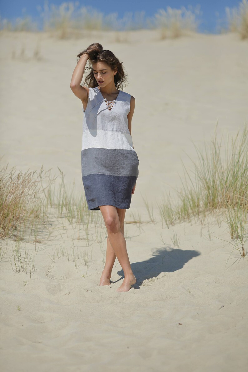 May include: A woman wearing a striped linen dress with a lace-up neckline, standing in a sandy desert landscape.