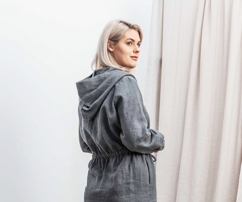 K&ouml;nnte beinhalten: Eine graue Kapuzenjacke aus Leinen mit Kordelzug in der Taille. Die Jacke ist aus einem weichen, leichten Stoff gefertigt und hat eine lockere Passform.