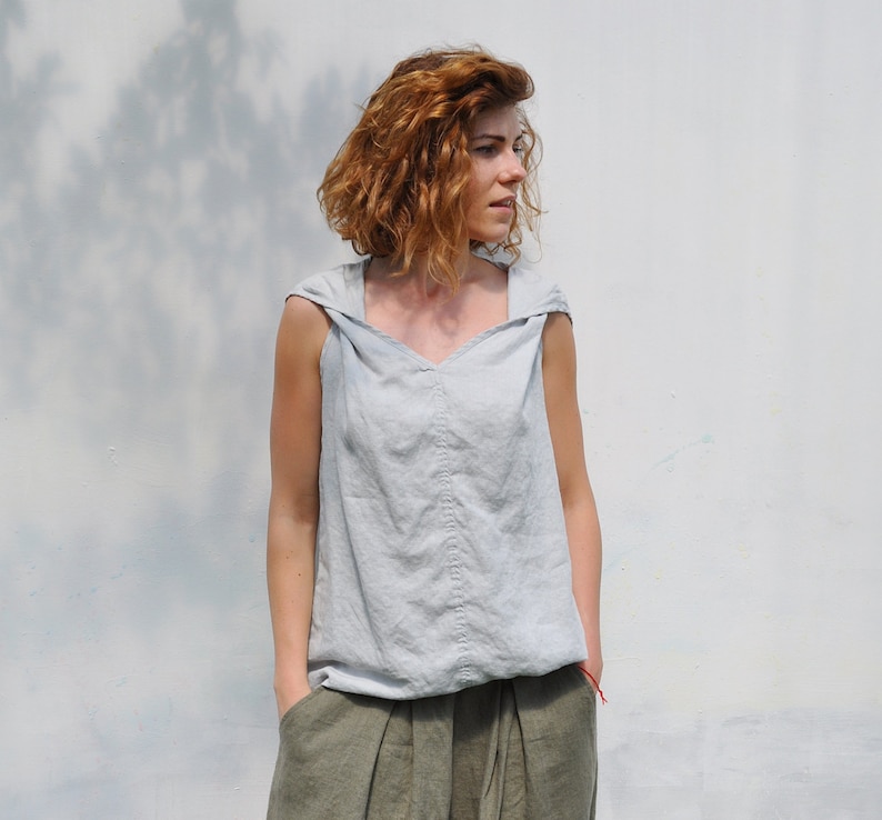 May include: A light gray sleeveless linen top with a hood and a V-neck. The top is made of a soft, lightweight fabric and has a relaxed fit.