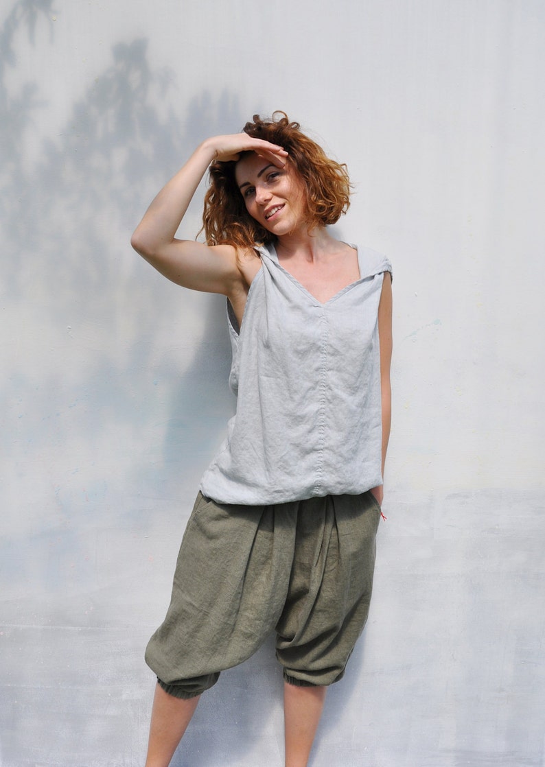 May include: A woman wearing a light gray sleeveless top with a v-neck and a pair of olive green linen pants.