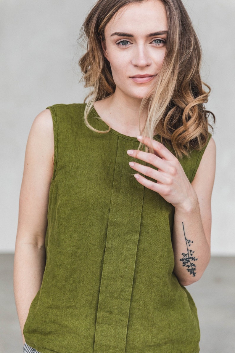 May include: A sleeveless, olive green linen top with a straight neckline. The top has a vertical seam down the front.