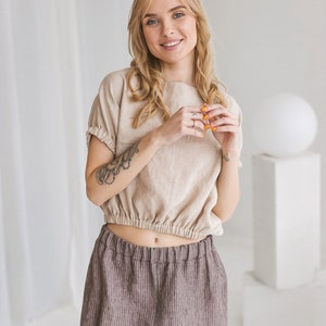 May include: A woman wearing a beige linen top with a gathered elastic waistband and brown striped linen pants.